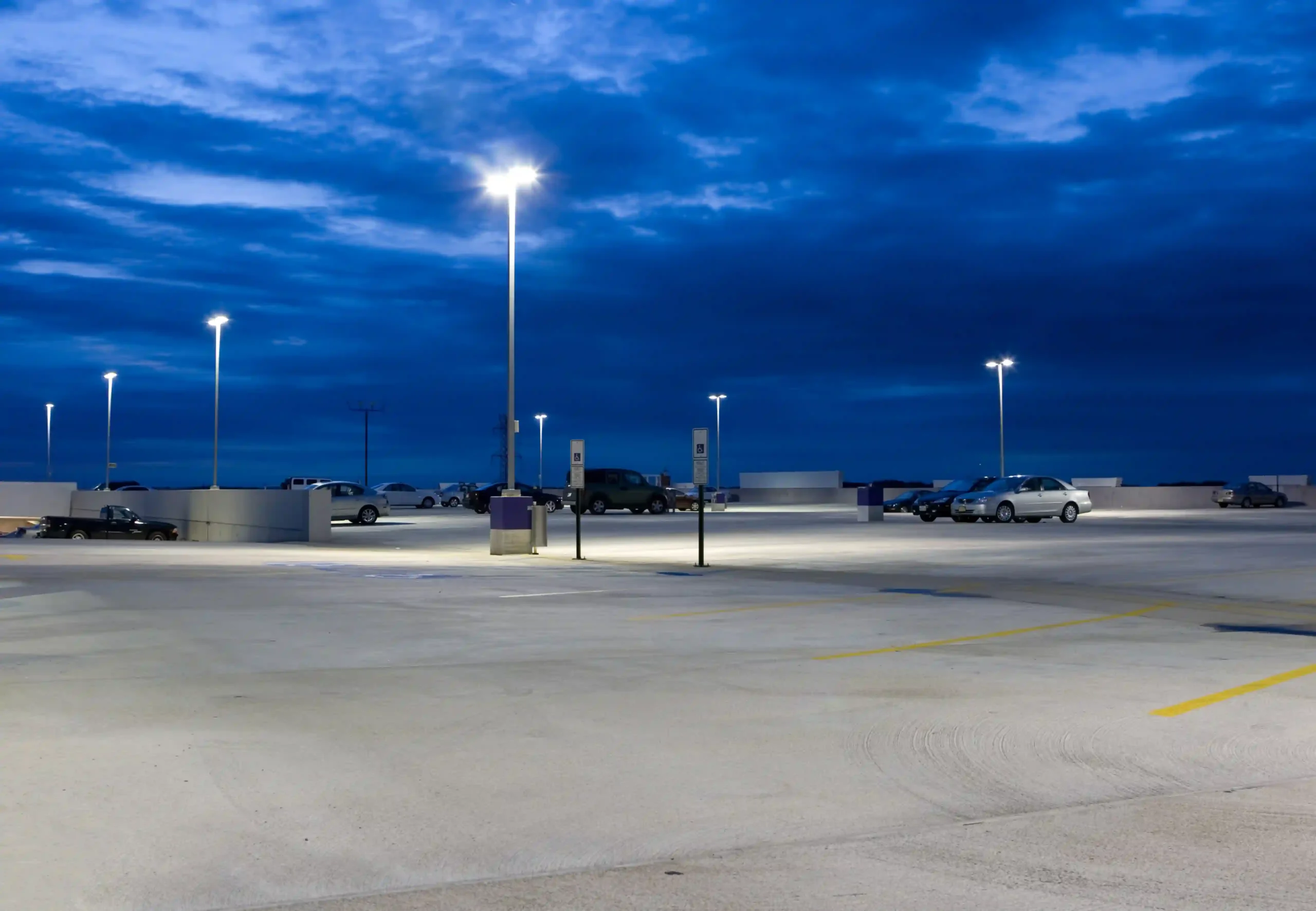 Parking lot with cracked pavement and damaged lighting, requiring repair and maintenance.